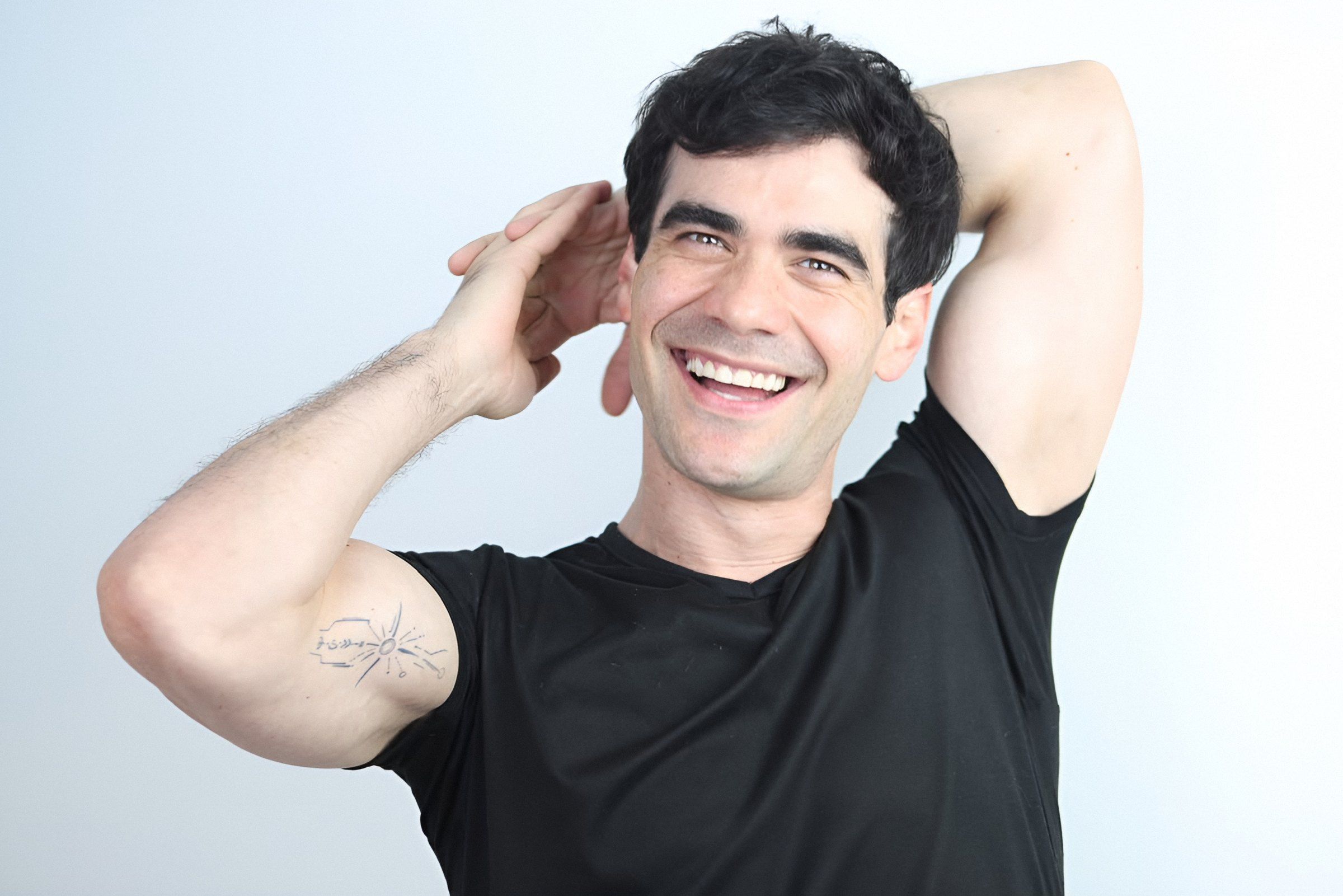 Germán Valdés de playera negra se ríe con los brazos detrás de la cabeza