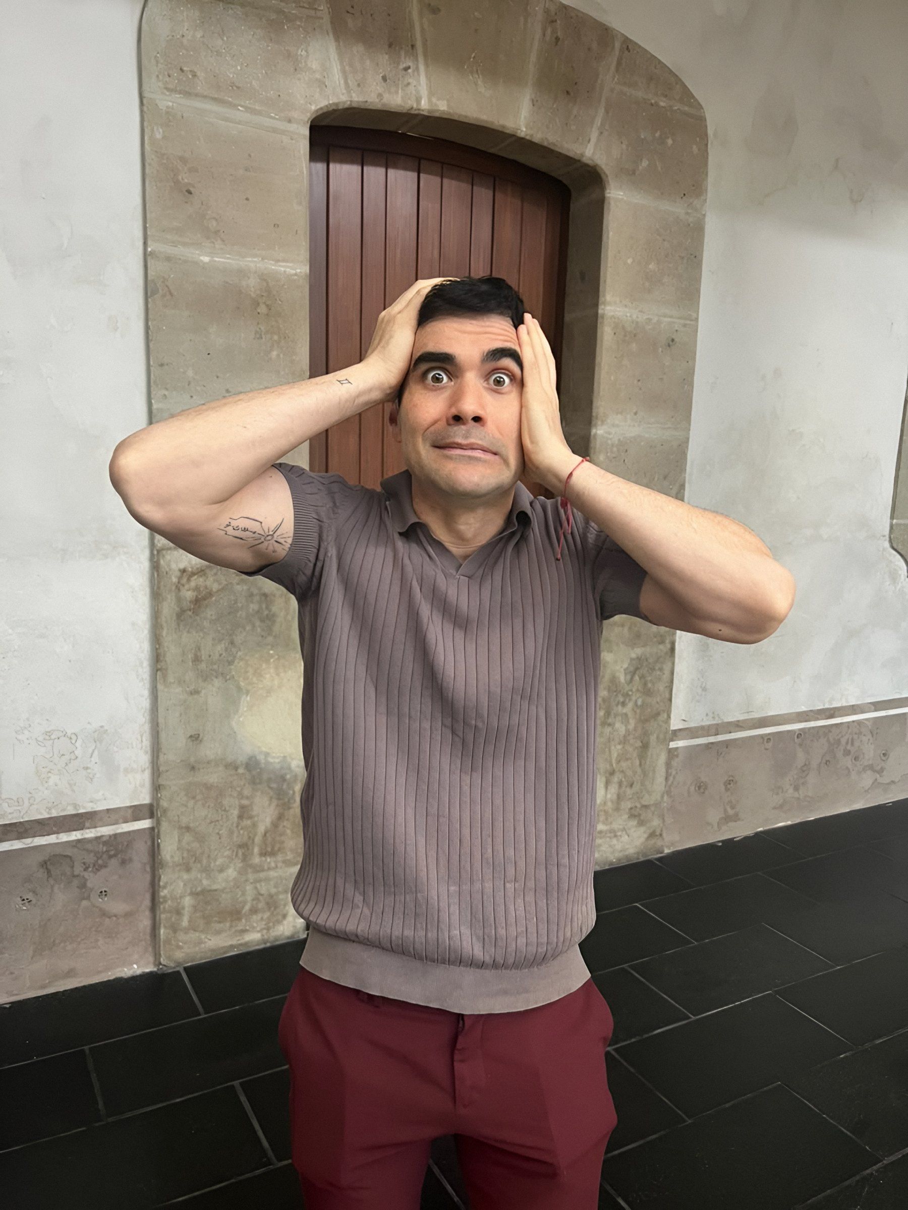 Germán Valdés se lleva las manos a la cabeza con cara de sorpresa frente a un portón de madera